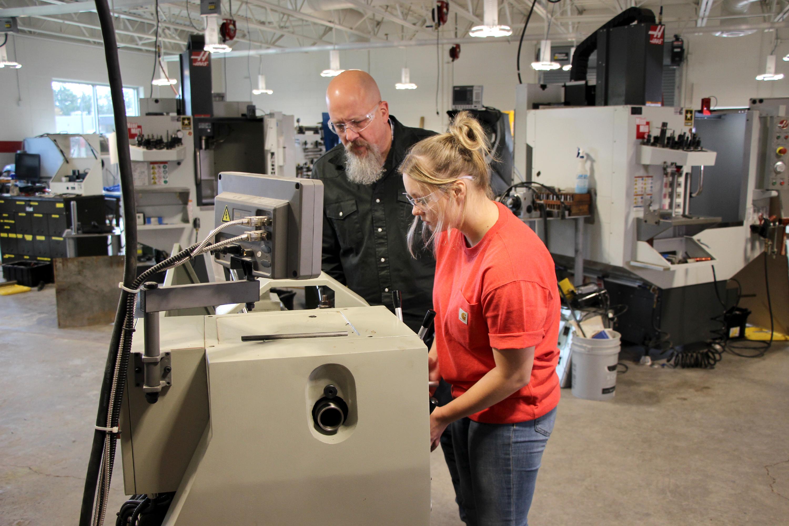 A student works on a machine while the instructor watches and offers help